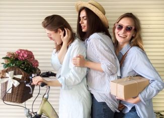 3 jeunes femmes posant sur un vélo avec des fleurs et un colis